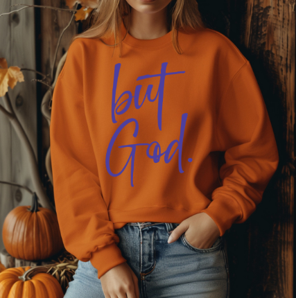 Woman wearing a burnt orange sweatshirt with yellow text reading 'but God', a popular Christian faith-based apparel."