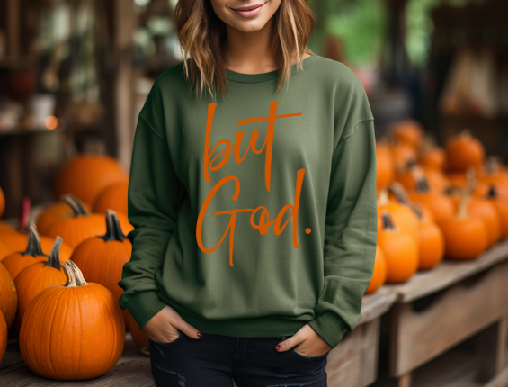 Woman wearing a military green  sweatshirt with yellow text reading 'but God', a popular Christian faith-based apparel."