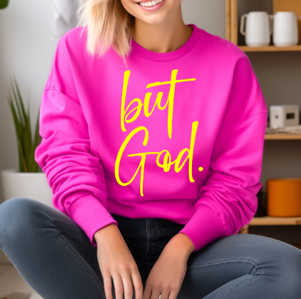 Woman wearing a bright pink sweatshirt with yellow text reading 'but God', a popular Christian faith-based apparel."