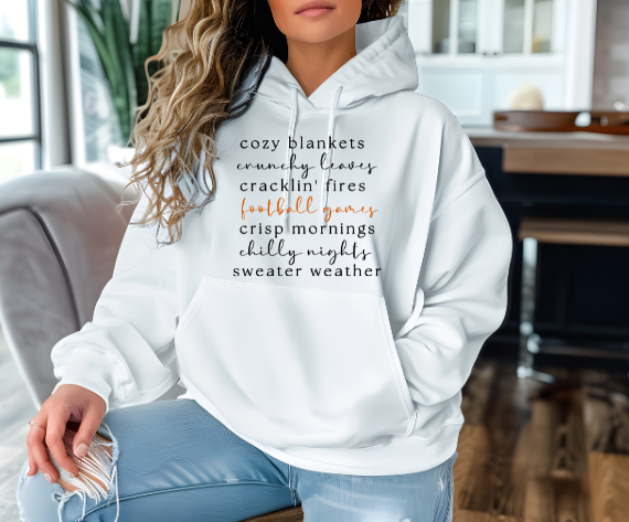 woman wearing a white hoodie with the text "cozy blankets crunchy leaves football games" trendy fall sweatshirt