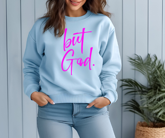 woman wearing a a light blue Christian themed sweatshirt that reads "but God." in hot pink font