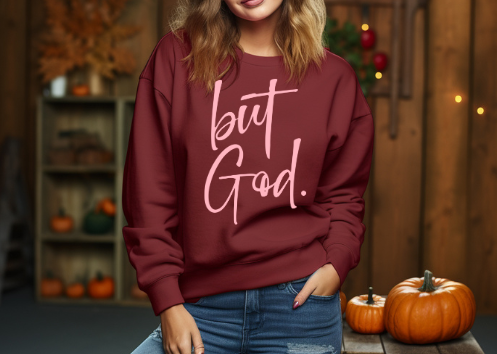 Woman wearing a maroon pink sweatshirt with yellow text reading 'but God', a popular Christian faith-based apparel."