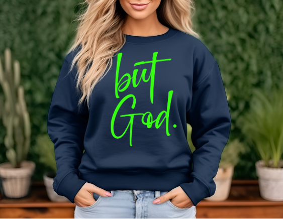 Woman wearing a navy   sweatshirt with green text reading 'but God', a popular Christian faith-based apparel."